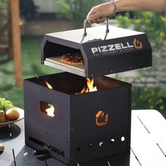 a person holding a pizza box over an open fire pit on top of a table