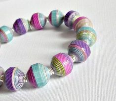 a close up of a bracelet made out of paper beads on a white table cloth