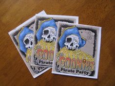 three stickers on a wooden table that say goonies pirate party and two skulls wearing hats