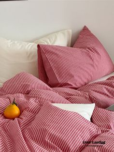 an orange sitting on top of a bed covered in red and white sheets with pillows