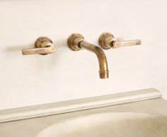 two brass faucets on the wall above a sink