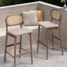 two wooden stools sitting next to each other on a cement wall near flowers and pillows