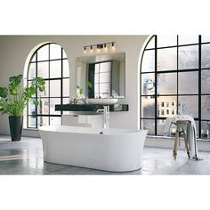 a large white bathtub sitting in front of two windows with potted plants next to it