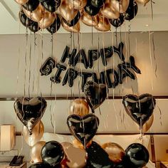 black and gold balloons with happy birthday written on them hanging from the ceiling in a room