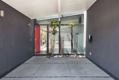 an entrance to a building with red doors and trees in the entryway, next to a concrete walkway