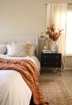 a white bed sitting next to a window with a vase filled with flowers on top of it