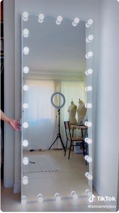 a large mirror with lights on it in a room next to a table and chair