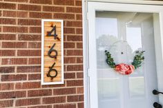 a house number sign on the side of a brick building with a wreath and flowers