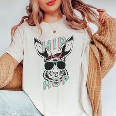 Get ready to groove into Easter with our "Hip Hop Ya Don't Stop Bunny Tee"! This fun and fashionable shirt comes alive with a cool bunny rocking a pair of shades, adding a touch of whimsy to your holiday look. It's crafted from premium materials, ensuring comfort and durability for all your spring adventures. Here’s why you’ll love it: Stylish Design: Rock a unique Easter look with a playful twist on your favorite seasonal icon. Quality Fabric: Enjoy a soft, breathable experience that keeps you Easter Tees, Unique Easter, Dont Stop, Rock A, Holiday Looks, Large White, Custom Clothes, Stylish Design, Exclusive Designs