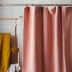 a pink shower curtain in a bathroom next to a yellow towel rack and white tiled walls