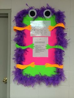 a bulletin board with purple and green feathers on it, two googly eyes in the middle