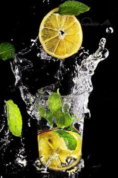 lemons and mint leaves splashing into a glass of water on a black background