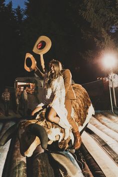 a man and woman riding on the back of a cow in an enclosure at night