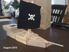 a pirate ship made out of popsicle sticks on a table with a brown paper bag in the background