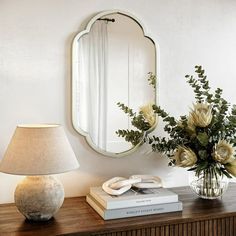 a vase with flowers sitting on top of a table next to a mirror and lamp