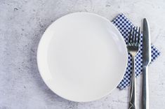 a white plate with a blue checkered napkin next to a silver fork and knife