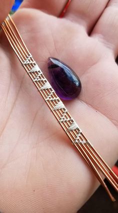 a person is holding a piece of jewelry in their hand and it's purple stone