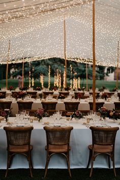 an outdoor tent with tables and chairs set up for a formal dinner or party, surrounded by string lights