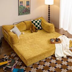 a yellow couch sitting on top of a wooden floor next to a lamp and pictures