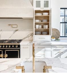 a white kitchen with marble counter tops and gold trimmings on the cabinet doors