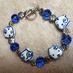 Hand Crafted Blue And White Silvertone Kitty Bracelet Cute Cobalt Blue And White Ceramic Kitty Beads With Flowers On Their Foreheads Alternate With Faceted Blue Glass Beads And Silvertone Flower Spacer Beads. Toggle Clasp Approximately 7 3/8 Inches Adorable Bracelet For Kitty Lovers! Designed And Handcrafted By Aj_nelly! Clay Charm Bracelet, Bracelet Supplies, Ceramic Beads Bracelet, Handmade Charm Bracelets, Clay Keychain, Bracelet Cute, Bracelet Inspo, Fotos Aesthetic, Clay Stuff