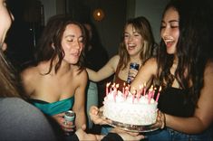 three women standing around a birthday cake with lit candles