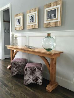 a wooden table with two stools underneath it and pictures on the wall behind it