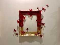 a gold framed mirror with red butterflies on the wall next to it in a white walled room