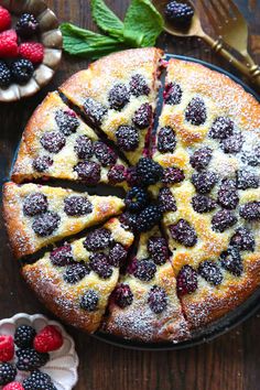 a cake topped with berries and powdered sugar on top of a wooden table next to other desserts