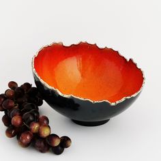 an orange and black bowl next to some grapes