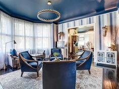 a living room filled with blue furniture and walls covered in striped wallpaper, along with a chandelier hanging from the ceiling