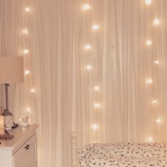 a bedroom with white curtains and lights on the wall