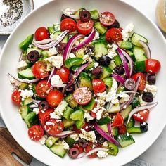 a salad with cucumbers, tomatoes, onions and olives in a white bowl