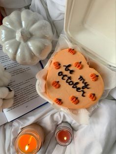 a cake with writing on it sitting next to candles and pumpkins in front of an open book