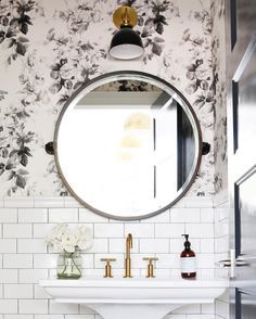 a white sink sitting under a round mirror in a bathroom next to a wall mounted faucet