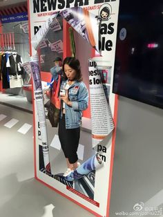 a woman looking at her cell phone in front of a news paper advertisement on display