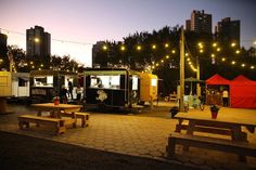 some food trucks are parked on the side of the road with lights strung over them