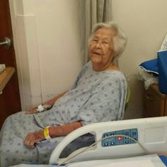 an elderly woman in a hospital bed with her hand on the handlebars and smiling