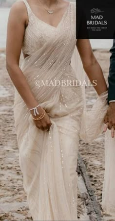 the bride and groom are walking together on the beach in their wedding attire, holding hands