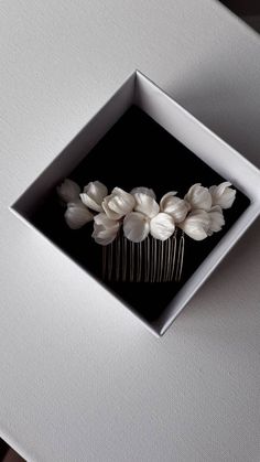 a hair comb with white flowers in a square box on top of a table next to a window