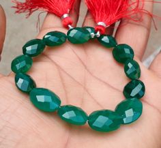 a person holding a green bracelet with red tassels on it's fingers