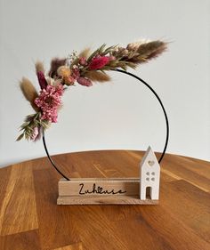 a small wooden house on top of a table with flowers in the middle and a name plate attached to it