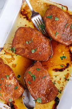 three pieces of meat on a white plate with a fork in it and sauce drizzled over them