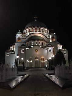 a large white building with lights on it's sides and fountains in the foreground