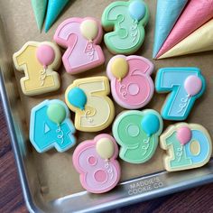 decorated cookies in the shape of numbers and balloons on a cookie sheet with cones to decorate them