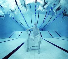 a man sitting on a chair in an indoor swimming pool with his legs spread out