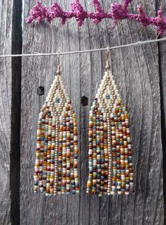 beaded earrings hanging from a clothes line on a wooden fence with purple flowers in the background