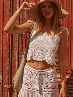 a woman standing in front of a red wall wearing a white top and skirt with crochet