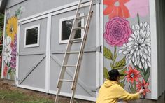 a woman is painting the side of a building with flowers on it and a ladder