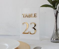 a table number is displayed next to a vase with flowers in it and a white plate